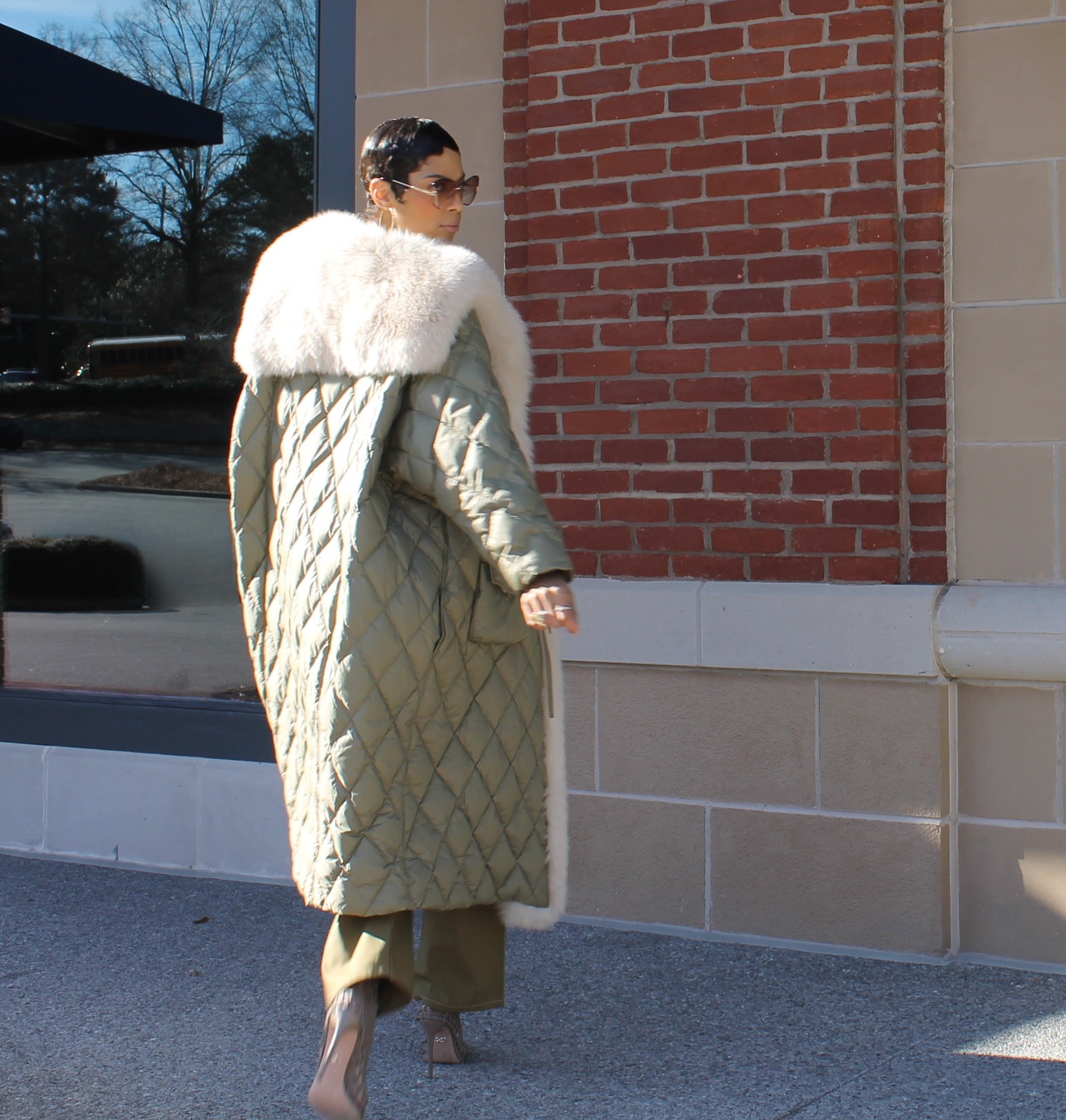 Woman wearing long down ultra lightweight Jade coat is crafted with goose down interior, exterior geometric quilting, enriched luxurious fox fur trim, and extended fur back flap.