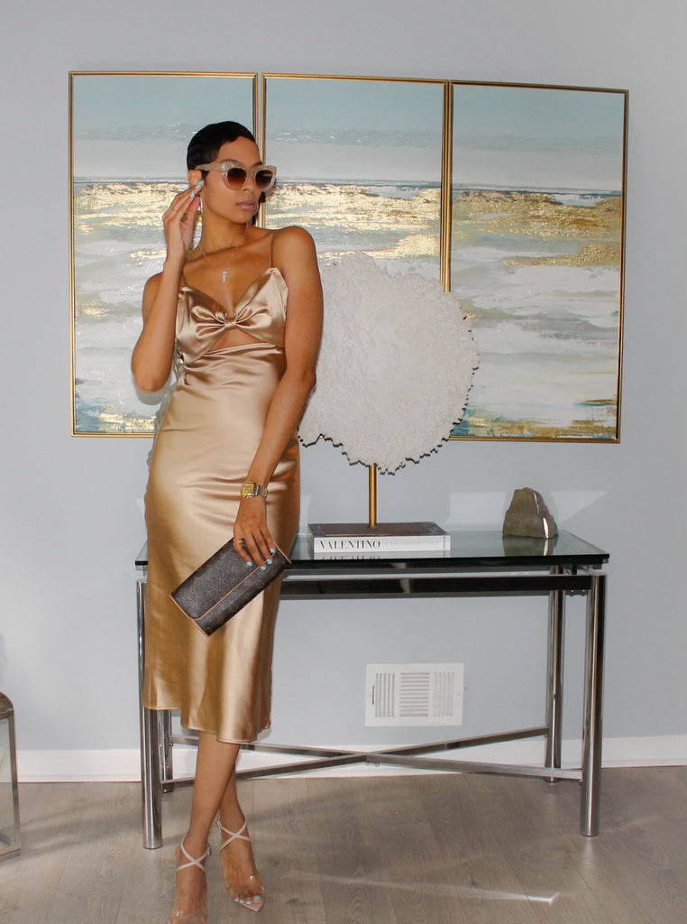 Front view of woman in champagne color midi length dress with V Neckline featuring subtle Bow Statement Detail with Peek-a-Boo Frontal Feature accompanied with adjustable spaghetti straps.